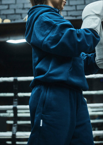 Person wearing a blue tracksuit in an indoor setting with a brick wall.